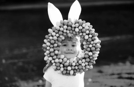 Foto de Niño de Pascua en orejas de conejo cazando huevos de Pascua al aire libre. Lindo niño en traje de conejo con orejas de conejo divertirse en el parque - Imagen libre de derechos