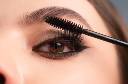 Photo for Closeup of eye makeup. Applying maskara on lushes Young woman getting make up with brush. Eyes visage woman - Royalty Free Image