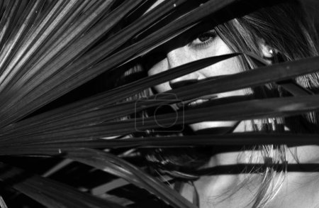 Téléchargez les photos : Portrait de femme tendre regardant hors de la feuille de palmier tropicale. Beauté visage gros plan - en image libre de droit