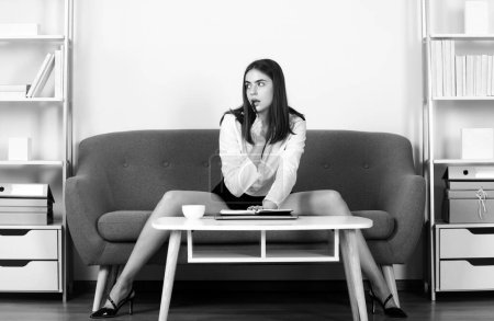 Foto de Seductora secretaria sexy freelancer con piernas sexy sentarse en el sofá en la oficina. Sexy mujer de negocios coqueteando - Imagen libre de derechos
