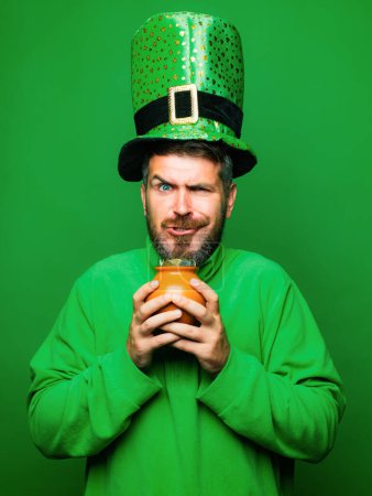 Mann im Heiligen Patricks Day Kobold Party Hut halten Topf mit Gold auf grünem Hintergrund. Happy st patricks day concept mit Topf voll Gold