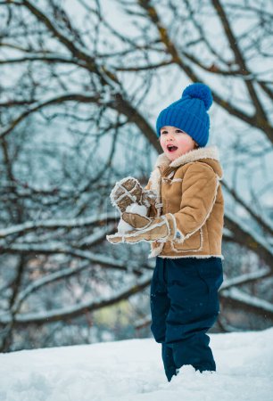 Foto de Retrato de invierno infantil. Lindo niño en el helado parque de invierno. Niño feliz jugando con nieve en una caminata invernal nevada. Niño de invierno. Personas en la nieve - Imagen libre de derechos