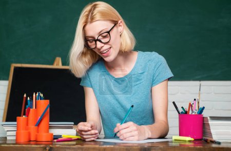 Young teacher in glasses over green chalkboard background. Portrait of creative young smiling female Student in glasses. Portrait of confident young Caucasian female teacher