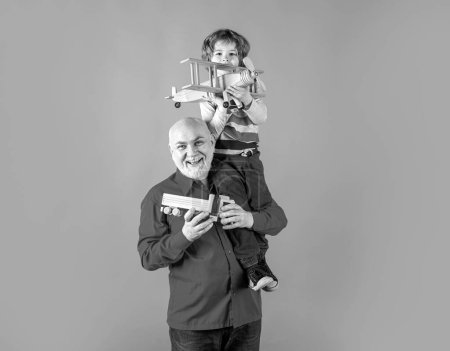 Téléchargez les photos : Grand-père et petit-fils piggyback avec avion jouet et camion en bois. Hommes génération grand-père et petit-enfant - en image libre de droit