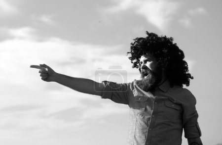 Photo for Crazy funny bearded man with black wig pointing finger on sky background. Funny facial expressions - Royalty Free Image