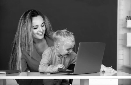 Photo for Mother and son together using computer laptop. Little school child son using laptop with mother. Teacher helping school kids in classroom at school - Royalty Free Image