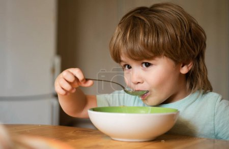 Niño comiendo comida saludable en casa. Feliz niño, desayuna. Retrato de un hermoso niño desayunando en casa. Sonriendo feliz adorable bebé comiendo puré de frutas en la cocina. Comer niños
