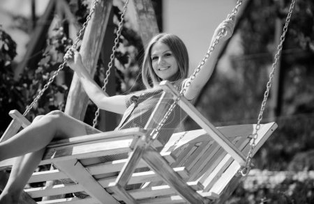 Photo for Gorgeous girl is swinging on a swing at nature garden. Outdoor portrait of a smiling happy girl. Young woman enjoying freedom and feeling carefree - Royalty Free Image