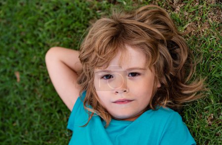 Cute boy lying in the grass. Handsome child enjoying on field or lawn and dreaming