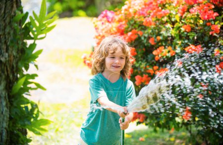 Foto de El niño feliz vierte agua de una manguera. Niños regando flores en el jardín. Jardinería doméstica - Imagen libre de derechos