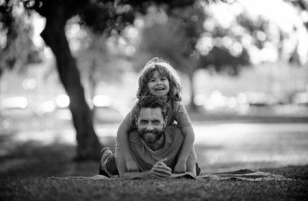 Foto de Sonriente padre e hijo tendidos en la hierba en el parque de verano al aire libre. La gente se divierte al aire libre. Concepto de vacaciones felices y familia amigable - Imagen libre de derechos