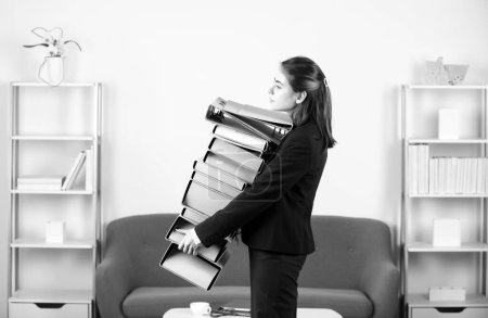 Foto de Joven empresaria sosteniendo muchas carpetas con los documentos con demasiado trabajo en la oficina. Secretaria chica - Imagen libre de derechos