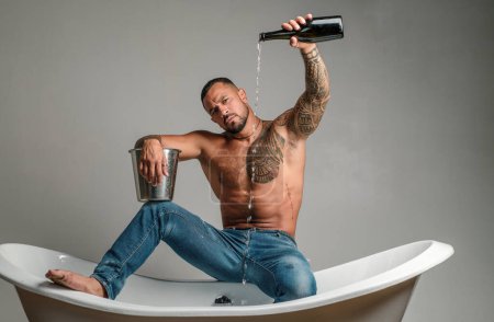 Foto de Hombre sexy sentarse en la bañera en el baño, los hombres de vacaciones con champán. Celebrando Navidad o cumpleaños. Fiesta de sexo privado - Imagen libre de derechos