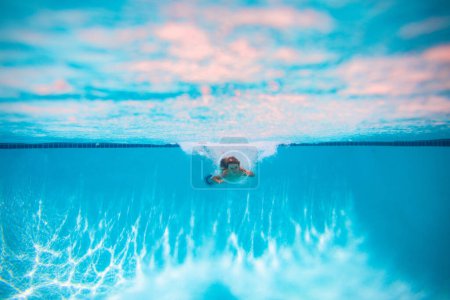 Téléchargez les photos : Enfant nager et plonger sous l'eau dans la piscine. Mode de vie sain et actif, activité sportive aquatique de natation pendant les vacances d'été avec l'enfant. Vacances d'été avec enfants - en image libre de droit