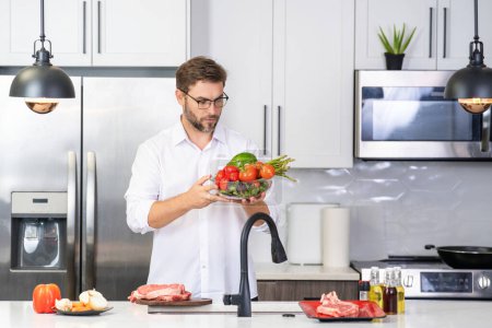 Photo for Middle aged man cooking in kitchen. Man on kitchen with vegetables. Portrait of casual man cooking in the kitchen with vegetable ingredients. Guy preparing salad at home in kitchen - Royalty Free Image