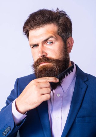 Téléchargez les photos : Homme barbu peignant la barbe. Gros plan d'un jeune homme coiffant sa longue barbe avec un peigne. Soin de barbe. Homme barbu avec barbe, gay barbu. Moustache hommes - en image libre de droit