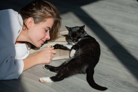 Téléchargez les photos : Une jeune femme joue avec un chat moelleux. Le chat est près du visage de la femme. Le chat noir moelleux s'est installé confortablement pour dormir ou jouer. Repose-toi. Mignon endroit confortable matin. Bonjour avec le chat à la maison. Le minou - en image libre de droit