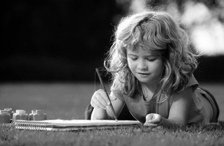 Téléchargez les photos : Jeune artiste peintre talentueux. Portrait d'un enfant heureux souriant appréciant l'art et le dessin artisanal dans la cour arrière ou le parc de printemps. Dessin pour enfants avec crayons en plein air - en image libre de droit