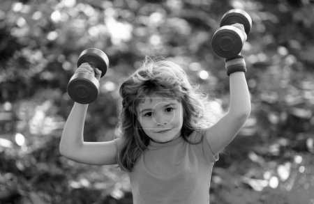 Photo for Kids sport. Boy is doing exercises to develop muscles. Child is doing exercises with dumbbells in park - Royalty Free Image