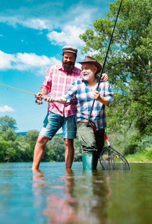 Foto de Padre e hijo maduro pescador pesca con una caña de pescar en el río - Imagen libre de derechos
