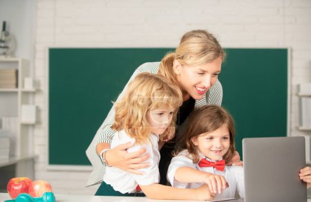 Photo for School teacher with a schoolkids learning at laptop computer, studying with online education. Teacher and little students in the classroom. Teacher and little students portrait, teachers day - Royalty Free Image