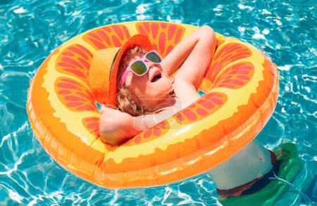 Téléchargez les photos : Portrait d'enfant amusant. Enfant dans la piscine sur anneau gonflable. Nage avec flotteur orange. Jouet aquatique, activité sportive de plein air saine pour les enfants. Enfants plage amusant - en image libre de droit
