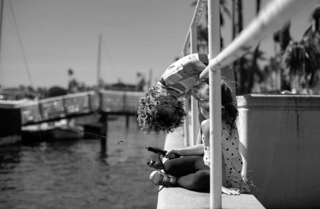 Junge, der sich mit Angeln beschäftigt, hält eine Angel in der Hand. Sommerlicher Lebensstil für Kinder. Kinder angeln am Wochenende. Zwei kleine süße Kinder angeln an einem sonnigen Sommertag auf einem See