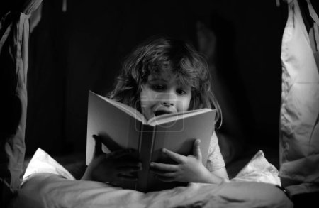 Foto de Un niño excitado leyendo un libro. Niños leyendo cuentos. Niños, hora de dormir. Niño leer libro en la cama - Imagen libre de derechos