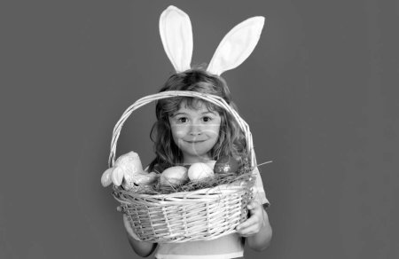 Photo for Bunny boy with easter basket isolated on blue background. Kids boy in bunny ears hunting easter eggs. Easter egg hunt. Funny kids face - Royalty Free Image