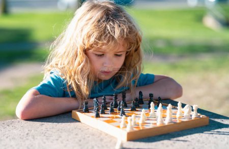 Téléchargez les photos : Pupil gamin penser à son prochain mouvement dans un jeu d'échecs. Petit garçon concentré assis à la table et jouant aux échecs - en image libre de droit