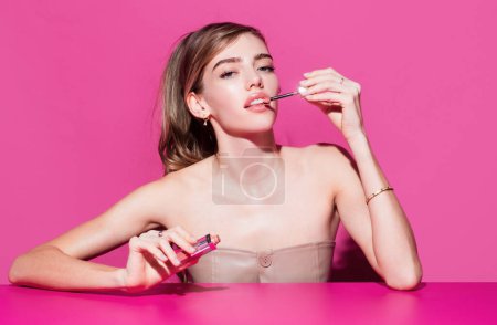 Sexy model applies pink lipstick on lips. Beautiful woman with beauty makeup and cosmetics. Girl model with perfect face skin and bright makeup portrait on pink background isolated