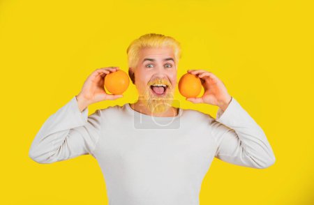 Foto de Man with orange fruit on orange background. Close up portrait young man holding sliced orange - Imagen libre de derechos