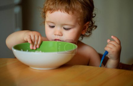 Photo for Kid baby eat soup in the kitchen with dishes and spoon - Royalty Free Image