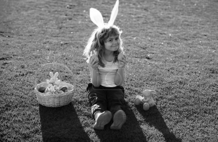 Téléchargez les photos : Enfant garçon avec des œufs de Pâques et des oreilles de lapin sur l'herbe. Enfants dans les oreilles de lapin sur la chasse aux œufs de Pâques dans le jardin - en image libre de droit