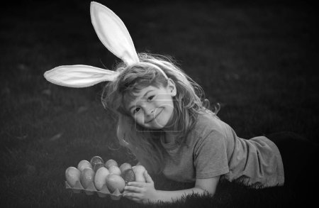 Téléchargez les photos : Enfant garçon en costume de lapin avec des oreilles de lapin chassant des œufs de Pâques. Lapin de Pâques enfants - en image libre de droit