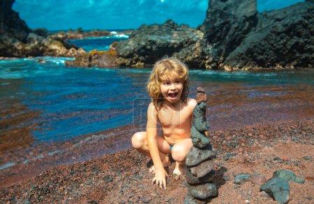 Téléchargez les photos : Enfant émerveillé excité faisant pyramide de pierres sur la plage de galets symbolisant la stabilité, zen, harmonie, équilibre - en image libre de droit