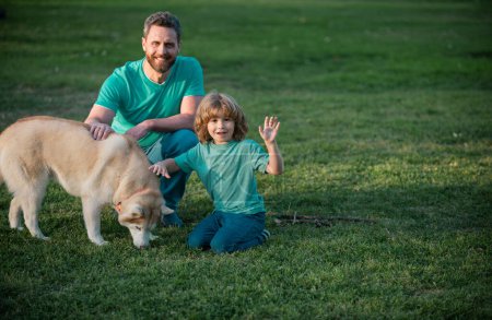 Téléchargez les photos : Fils et père en famille avec chien jouant ensemble dans le parc d'été sur l'herbe. Enfant avec son ami animal - en image libre de droit