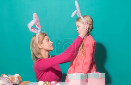 Happy family preparing for easter. Mother and her daughter child girl wearing bunny ears isolated on blue