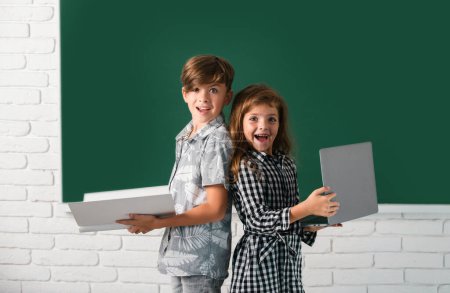 Foto de Niños niño y niña con computadora portátil y libro en la escuela - Imagen libre de derechos