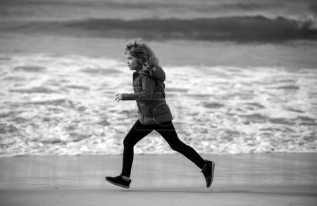 Téléchargez les photos : Enfant sportif courant dans la nature. Des enfants qui jouent sur la plage. Les enfants jouent en mer pendant les vacances d'été en famille. Du sable et de l'eau, de la protection solaire. Petit enfant courant et sautant au bord de l'océan - en image libre de droit
