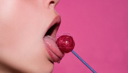 Photo for Mouth licking lollipop, red female glossy lips and pink candy lollipop isolated on pink - Royalty Free Image