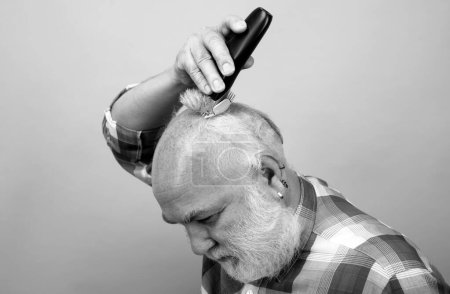 Senior con cortadora de cabello. Viejo hombre calvo cortador de pelo, calvicie madura y concepto de pérdida de cabello