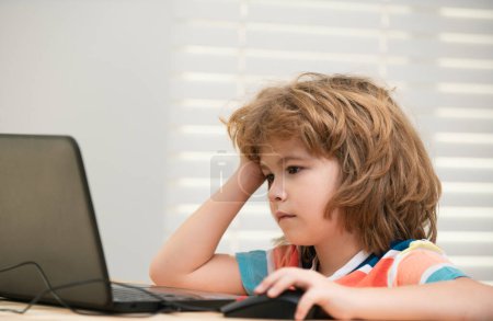 Téléchargez les photos : Portrait d'un écolier regardant l'ordinateur portable pendant la leçon. Éducation et apprentissage des enfants - en image libre de droit