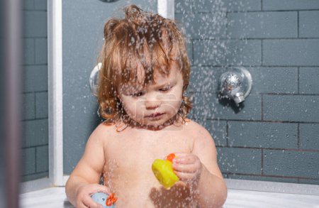 Foto de El niño se baña en una ducha. Lavando adorable bebé en el baño. Niño con jabón en el pelo tomando baño. Cuidado de la salud e higiene infantil - Imagen libre de derechos