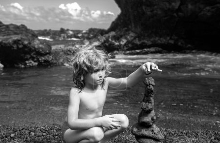 Téléchargez les photos : Petit garçon mignon faisant des pierres empilables sur la côte de la mer dans la nature. Cairn sur la plage de l'océan, cinq cailloux tour. Concept d'équilibre et d'harmonie. Calme et esprit - en image libre de droit