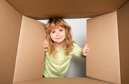 Photo for Kid boy unpacking and opening carton box looking inside with surprise face. Parcels and delivery - Royalty Free Image