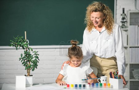 Photo for Schoolgirl drawing with teacher. Children from elementary school study at draw lesson. Pupil girl with mother teacher painting. School education and children concept - Royalty Free Image