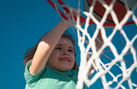 Téléchargez les photos : Gros plan image de l'enfant joueur de basket-ball faisant slam dunk pendant le jeu de basket-ball, photo de stock. Bannière isolée sur fond de ciel - en image libre de droit