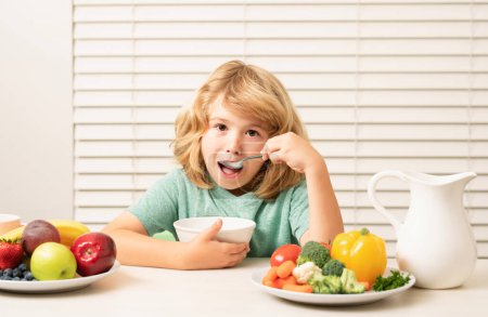 Téléchargez les photos : Kid preteen boy in the kitchen at the table eating vegetable and fruits during the dinner lunch. Healthy food, vegetable dish for children - en image libre de droit