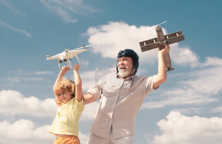 Téléchargez les photos : Enfant garçon et grand-père tiennent l'avion et drone quad copter contre le ciel. Enfant pilote aviateur rêvant de voler - en image libre de droit